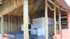 Un espace extérieur abrité, doté d’un toit de chaume, de piliers en bois et d’un banc rembourré.
