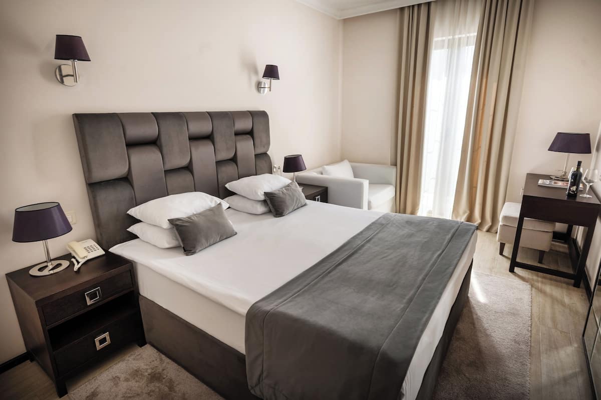 Una habitación de hotel con una cama grande, mesitas de noche, un escritorio y una silla.