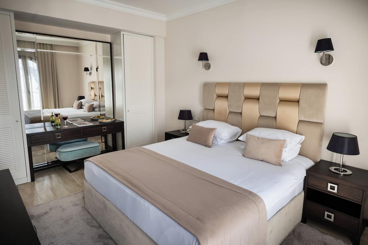 A hotel room with a large bed, a desk with a chair, a mirror, and two bedside tables with lamps.