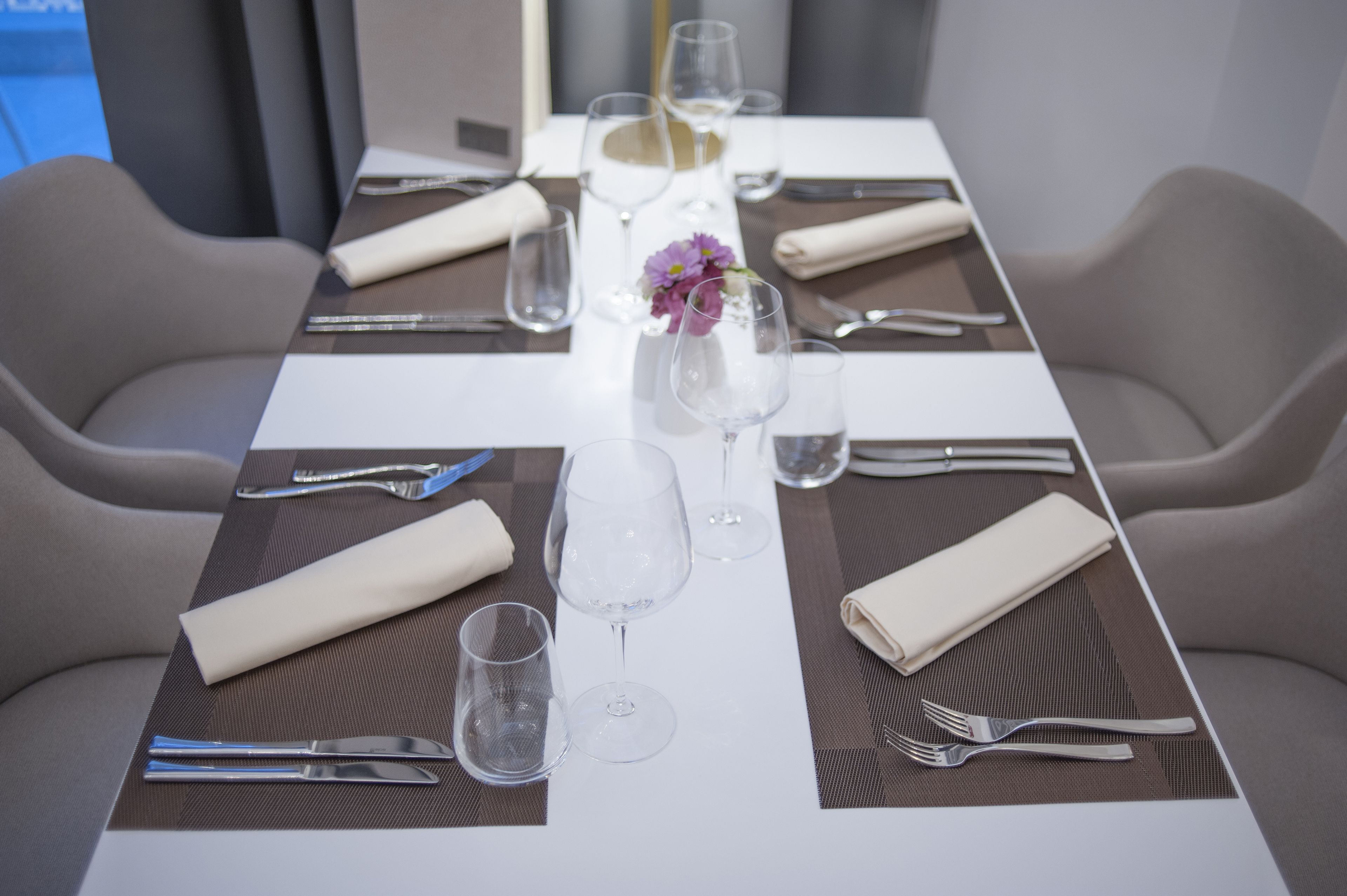 Una mesa de comedor bien puesta con un jarrón de flores, vasos traslúcidos y servilletas dobladas.