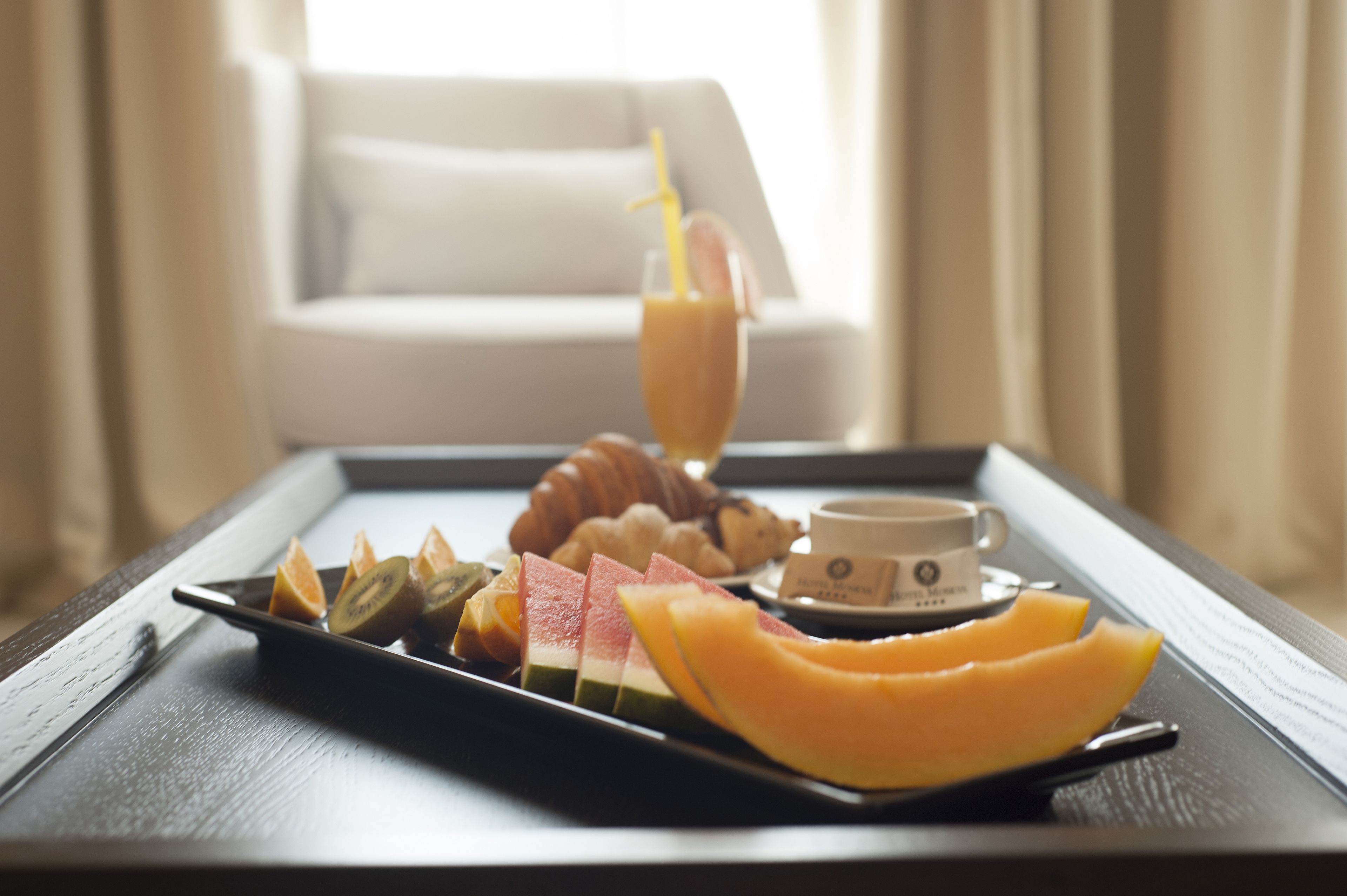 Un plateau avec des fruits coupés en tranches, un croissant, un verre de jus de fruits et une tasse de café, le tout posé sur une table en bois.