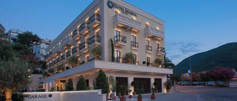 A multi-story hotel with balconies, a garage entrance, and potted plants.