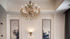 Una sala de estar con una araña, un sofá, dos sillones, una mesa de centro y dos obras de arte enmarcadas en la pared.