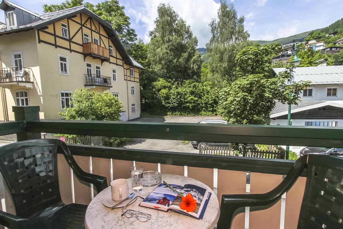 A balcony with a table set for two, featuring a book, a flower, and glasses.