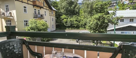 A balcony with a table set for two, featuring a book, a flower, and glasses.