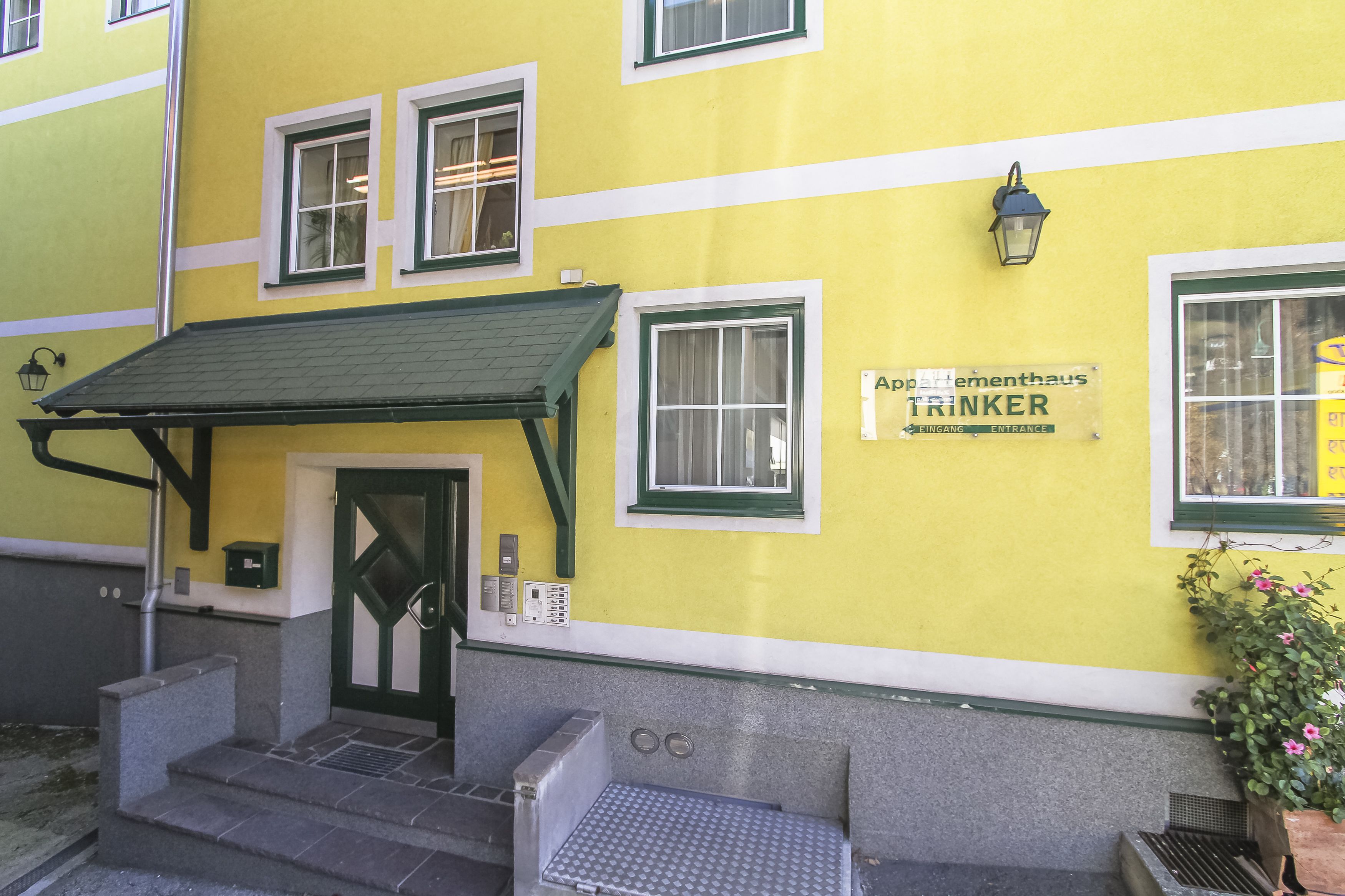 Un bâtiment jaune avec un auvent vert, une porte et une enseigne sur laquelle on peut lire « Apothekehaus TRINKER ».