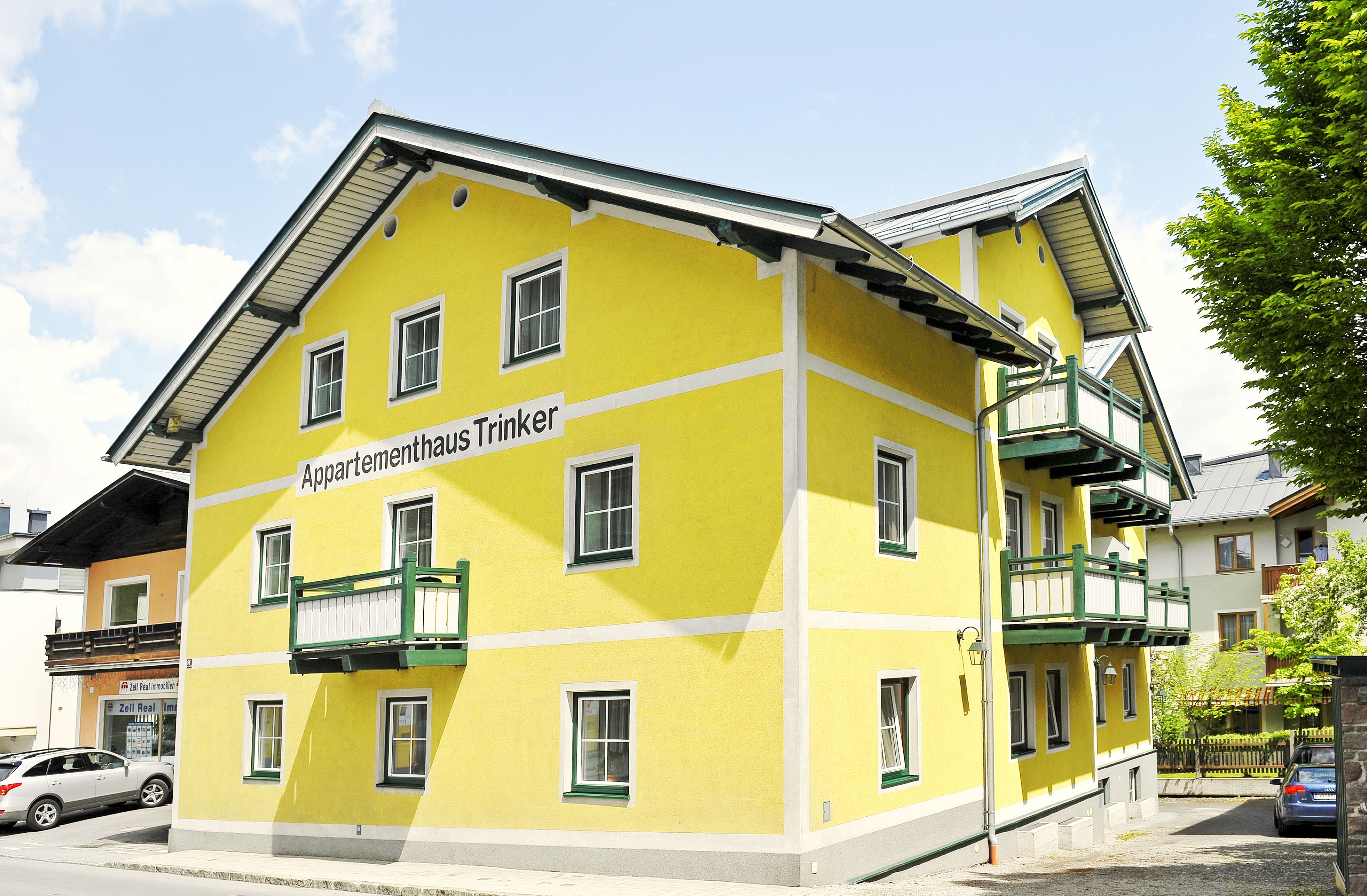 A yellow multi-story building with balconies and a sign reading "Appartementhaus Trinker".