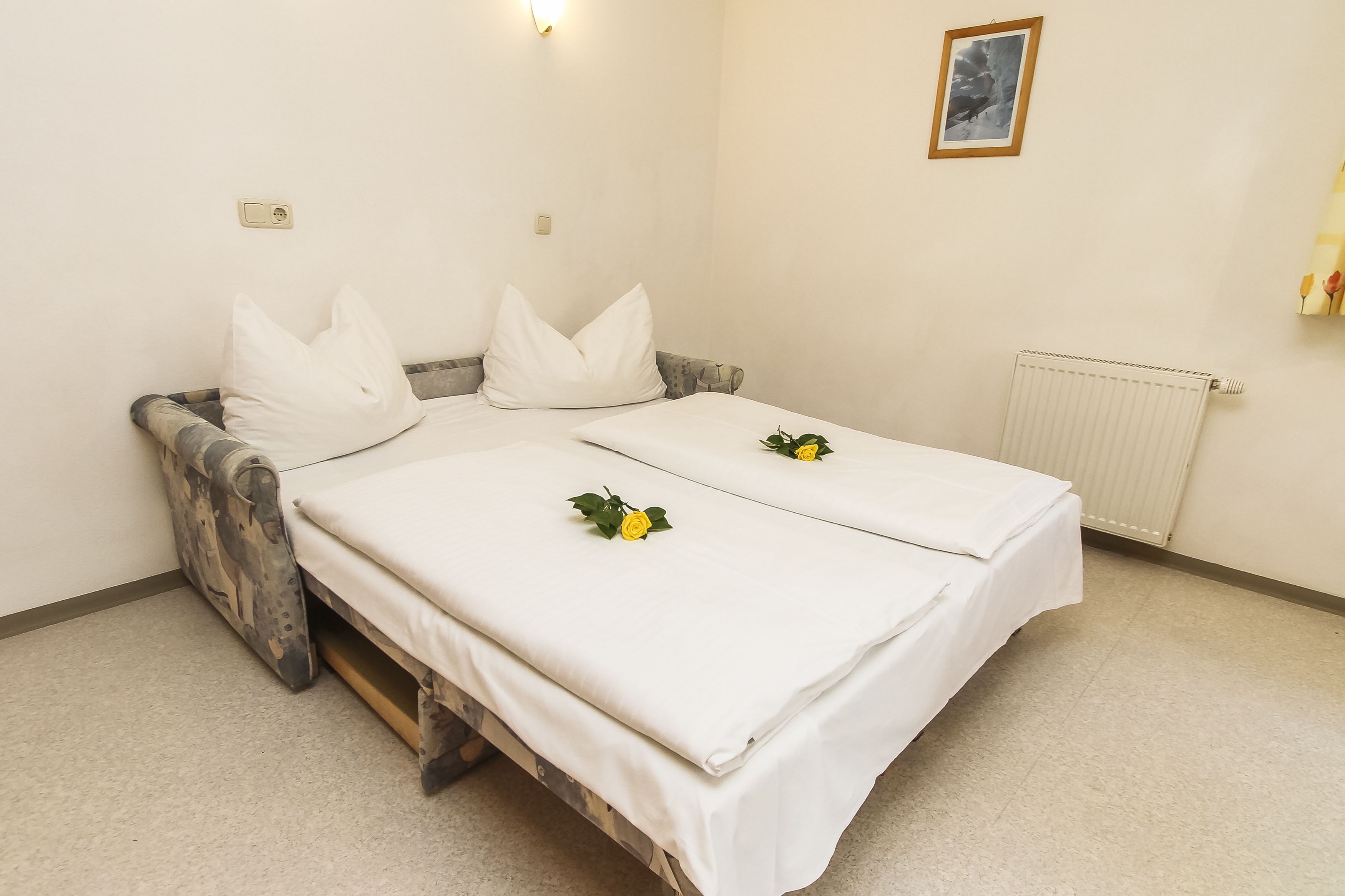 A double bed with white linens, two pillows, and a small yellow flower on each bed.