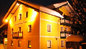 A yellow building with multiple windows and a balcony, surrounded by snow. - Appartements Trinker (Zell am See)