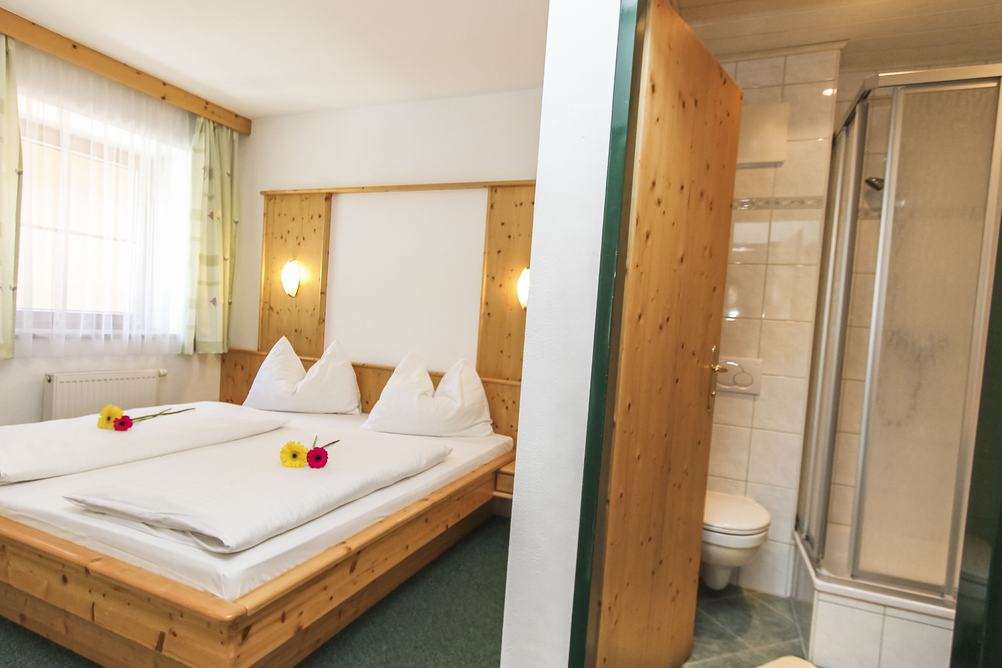 Una cama de madera con sábanas y almohadas blancas, un cabecero de madera y una ventana con cortinas traslúcidas.