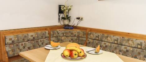 A dining area with a wooden table, cushioned bench, and a fruit bowl.