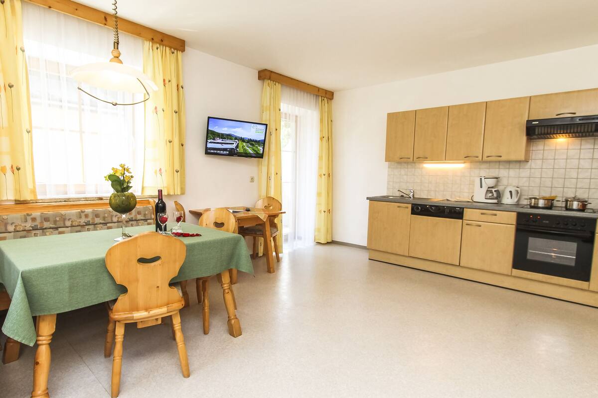 A dining area with a green tablecloth, wooden chairs, and a television on the wall.