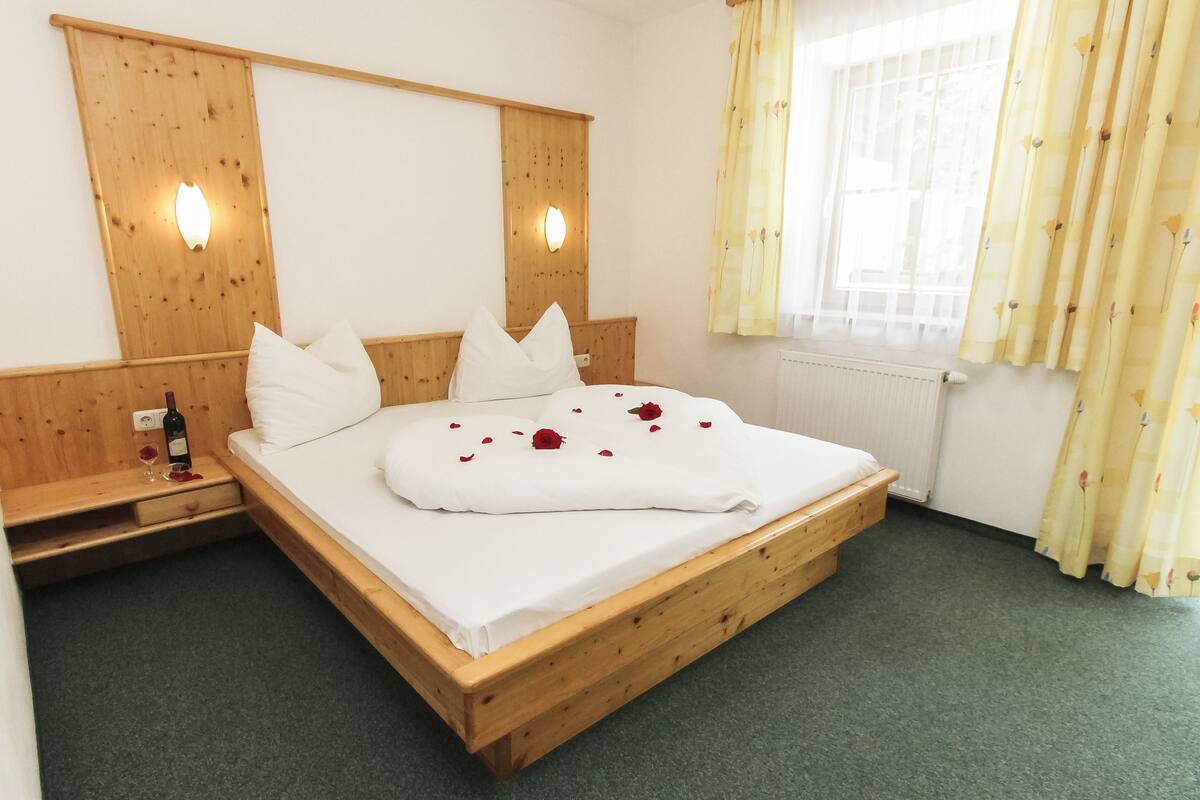 A wooden bed with white bedding, a nightstand, and a bottle of wine.
