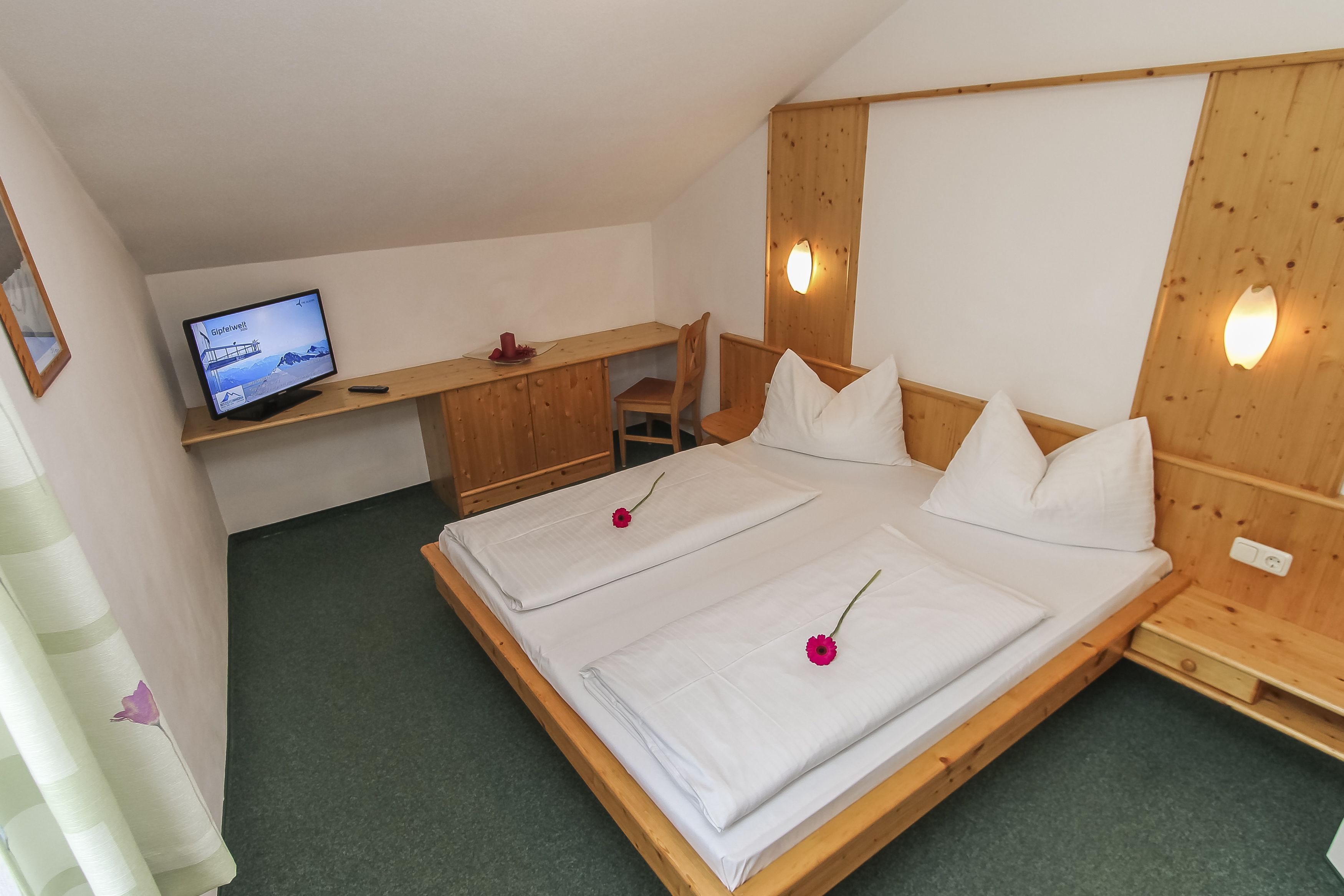 A room with a bed, a desk, a television, and a wooden wall panel.