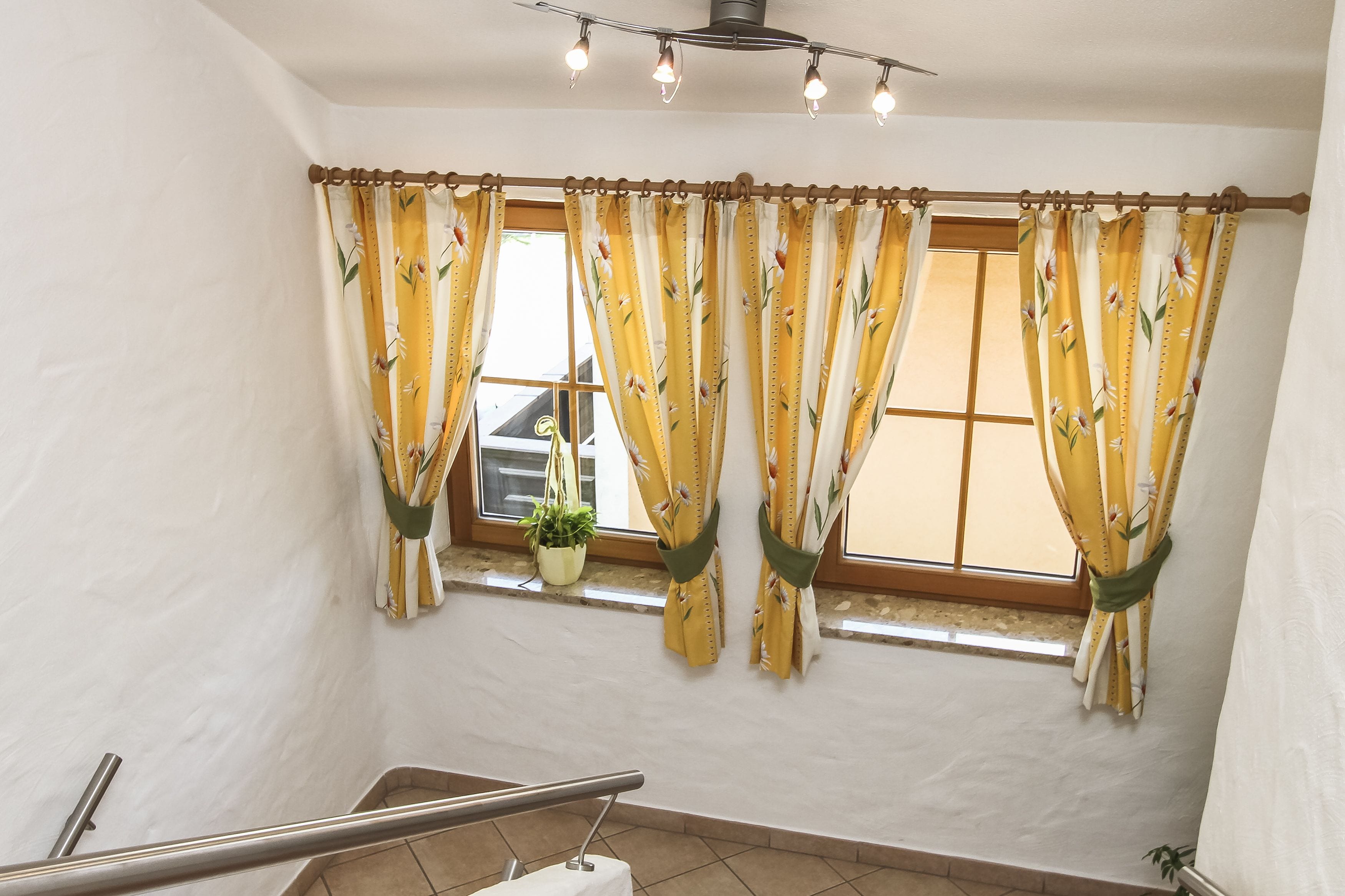 A staircase with a handrail, a window with yellow floral curtains, and a potted plant on the windowsill.