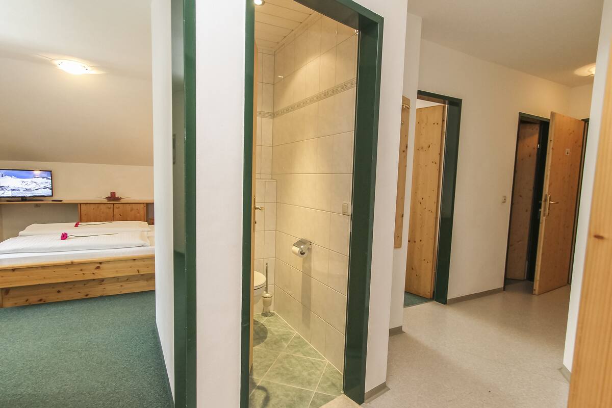 A hotel room with a bed, a television, a shower, and a hallway leading to other rooms.