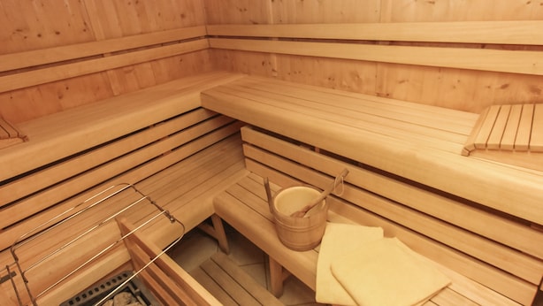 A wooden sauna with benches and a wooden bucket. - Appartements Trinker (Zell am See)