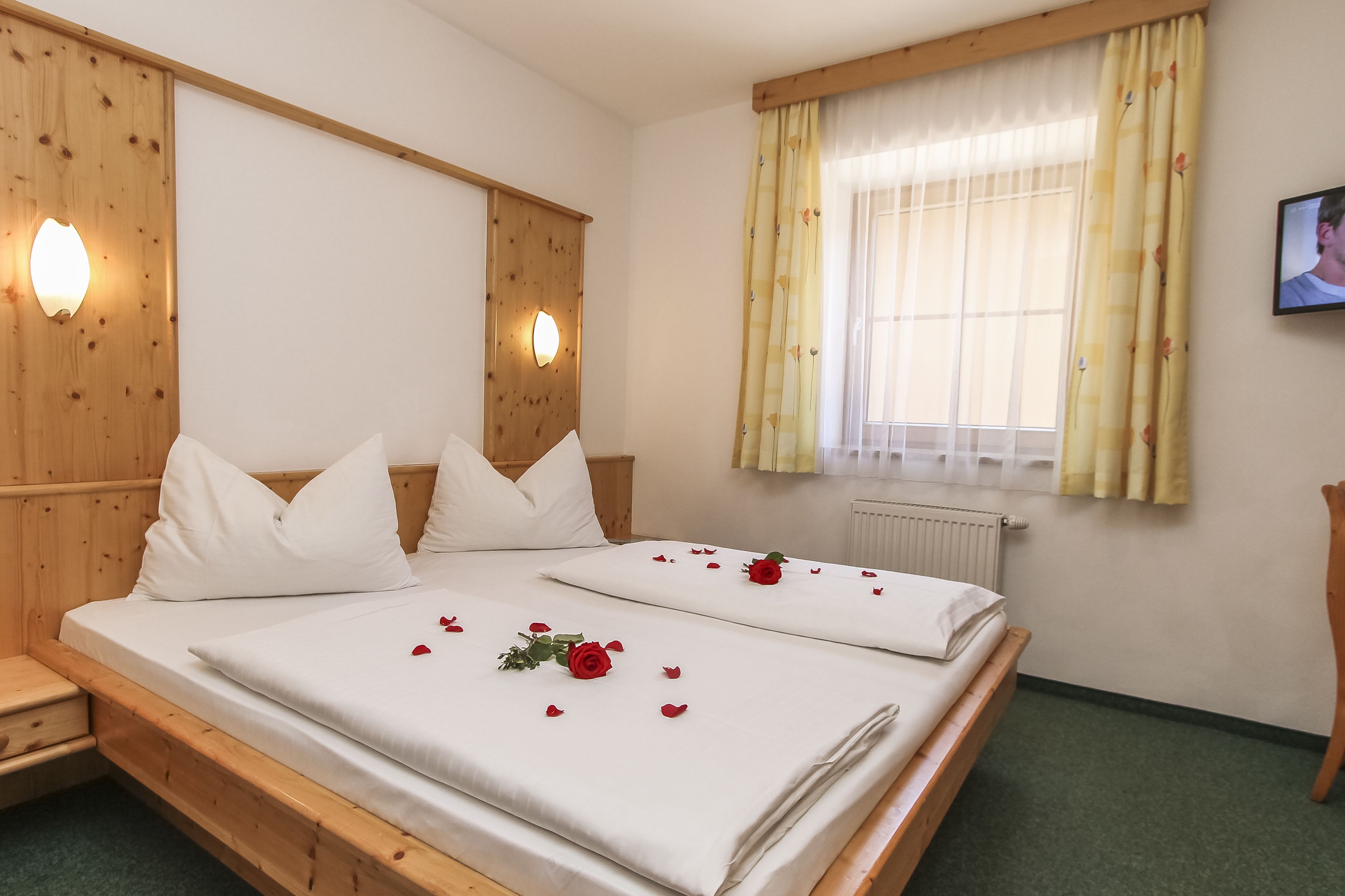 Una cama doble con sábanas blancas, dos almohadas y pétalos de rosa.