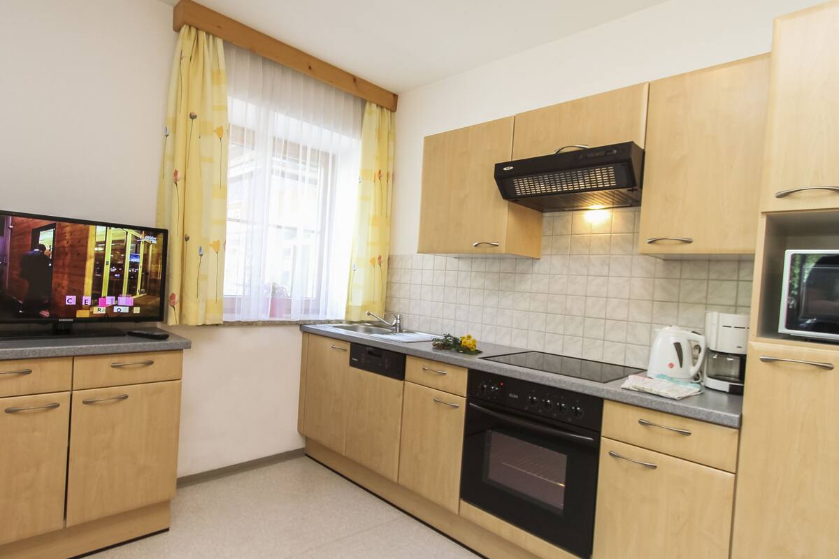 A kitchen with wooden cabinets, a dishwasher, an oven, a microwave, and a window with yellow curtains.