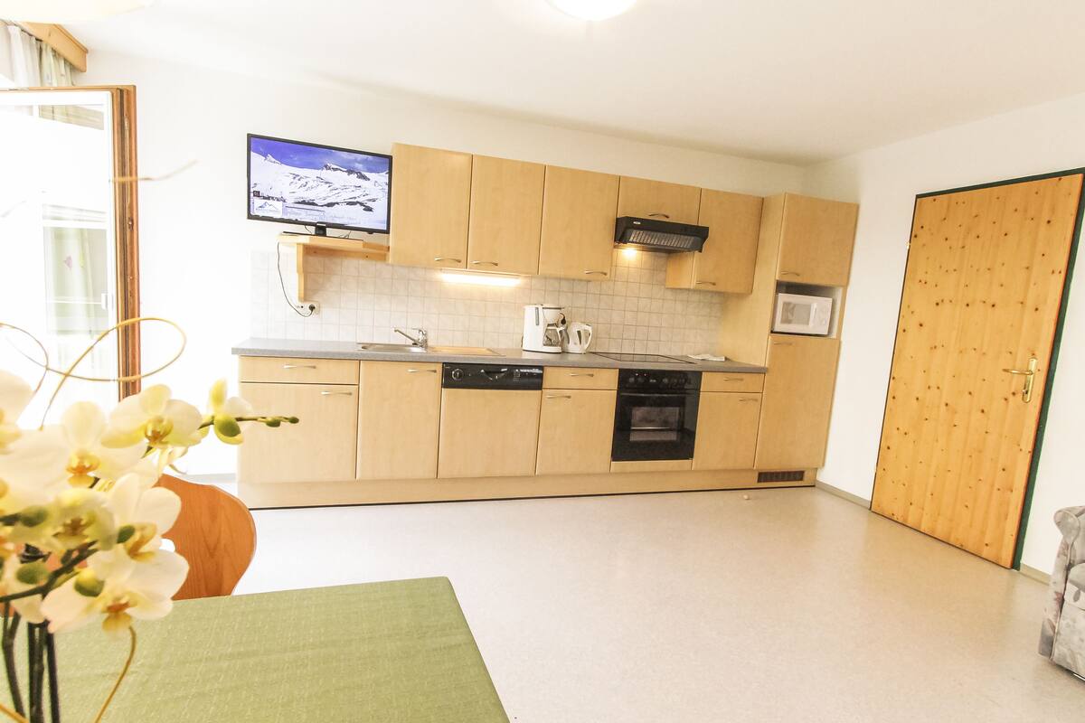 A modern kitchen with wooden cabinets, a dishwasher, an oven, and a television mounted above the counter.