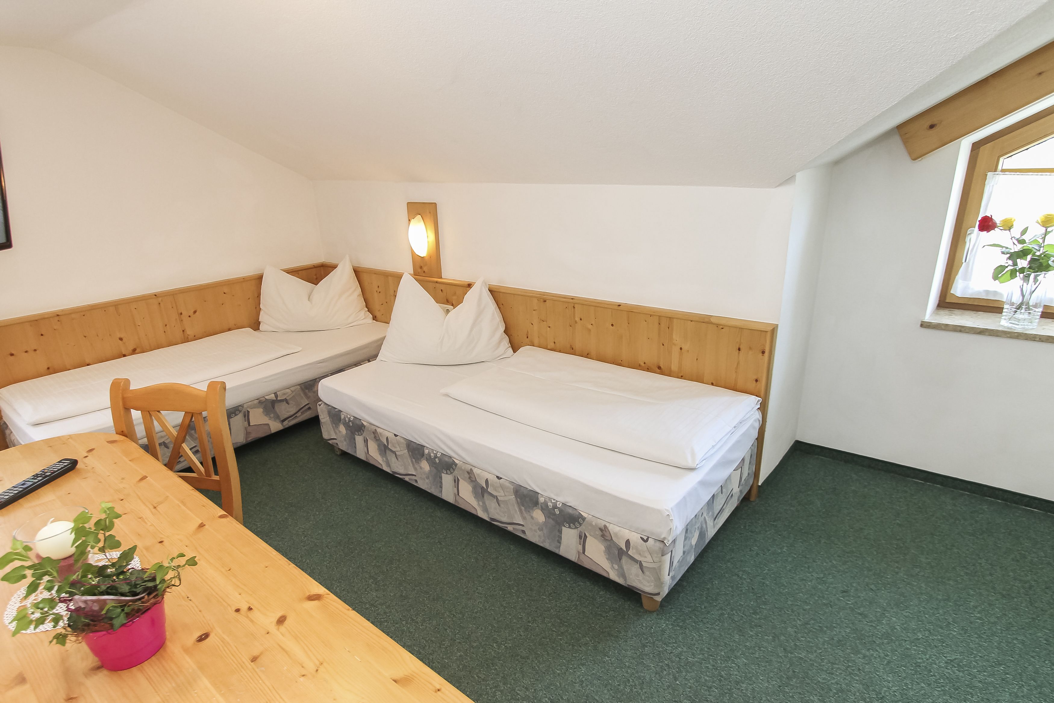 A room with two single beds, a wooden table, a chair, a remote control, and a potted plant.