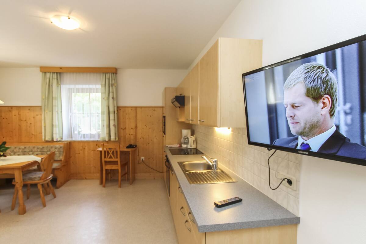 A modern kitchen with wooden cabinets, a built-in sink, and a flat-screen TV mounted on the wall.