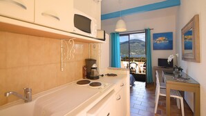 Una cocina compacta con estufa, microondas y cafetera. Se observa un área de comedor con mesa y sillas, con una vista panorámica a través de un ventanal.