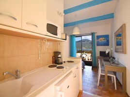 Una cocina compacta con estufa, microondas y cafetera. Se observa un área de comedor con mesa y sillas, con una vista panorámica a través de un ventanal.
