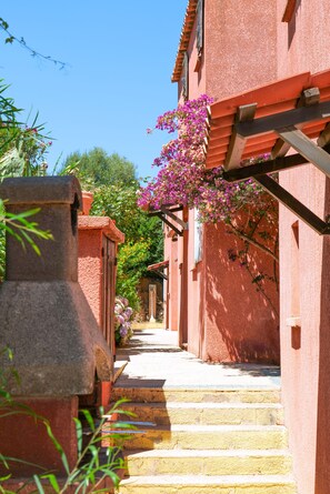A narrow street with steps leading to a building with a red facade and a stone structure on the left. - Le Maquis Bella Vista (Propriano)