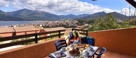 A terrace with a table set for breakfast, overlooking a scenic view of mountains and a lake.