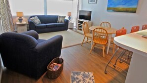 Un salon comprenant un canapé, un téléviseur, une table à manger avec des chaises et un tableau accroché au mur.