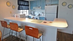 Une cuisine compacte dotée d’un îlot central, de tabourets de bar, d’une cuisinière, d’un réfrigérateur et de meubles de couleur bleu clair.