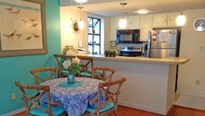 A compact kitchen with a central island, wooden chairs, and a dining table with a blue patterned tablecloth. - Lake Arrowhead Pad (Myrtle Beach)