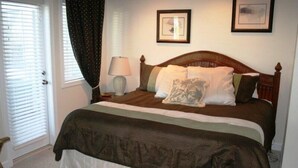 A bedroom with a wooden bed, a nightstand with a lamp, and two framed pictures on the wall. - Lake Arrowhead Quarters (Myrtle Beach)