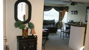 A doorway leading to a living room with a sofa, a coffee table, and a dining area with a chair and table. - Lake Arrowhead Quarters (Myrtle Beach)