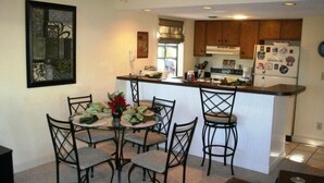 A compact kitchen with a dining area, featuring a central island, wooden cabinets, and a refrigerator with magnets. - Lake Arrowhead Quarters (Myrtle Beach)