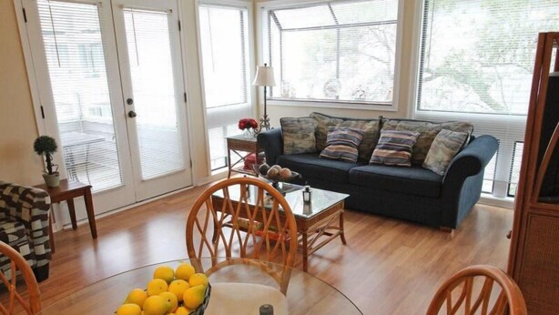 A living room with a sofa, chairs, a glass table with a fruit bowl, and a view through large windows. - Lake Arrowhead Element (Myrtle Beach)