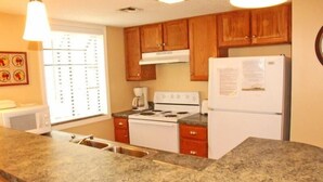 A kitchen with granite countertops, a stove, a refrigerator, wooden cabinets, and a window with blinds. - Lake Arrowhead Turf (Myrtle Beach)