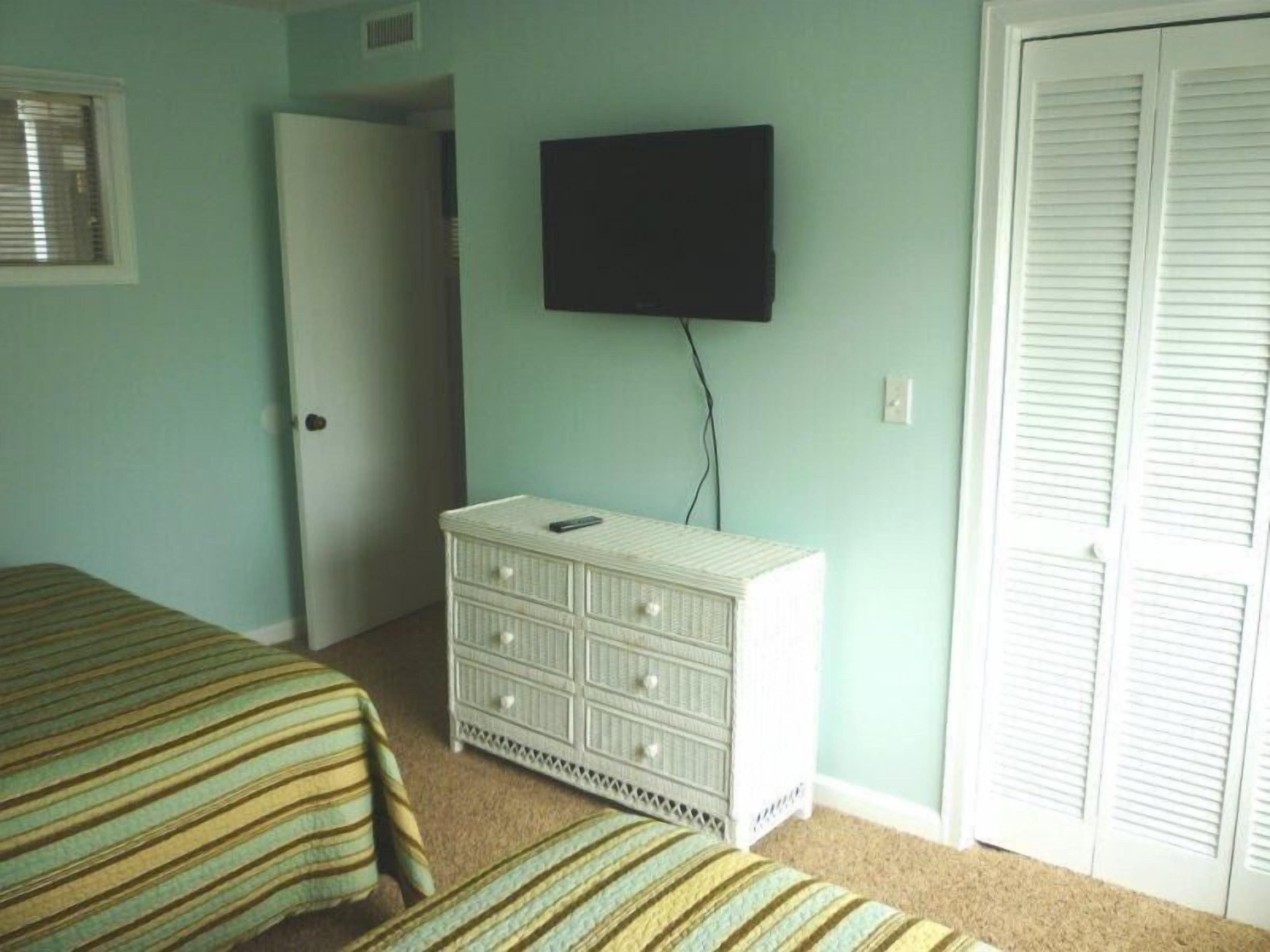A bedroom with two beds, a dresser, a television, and a closet.