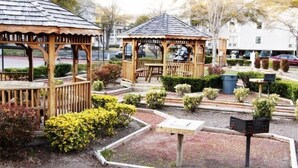 A gazebo with a wooden structure and a bench, surrounded by well-maintained bushes and a small garden area. - Lake Arrowhead Layaway (Myrtle Beach)