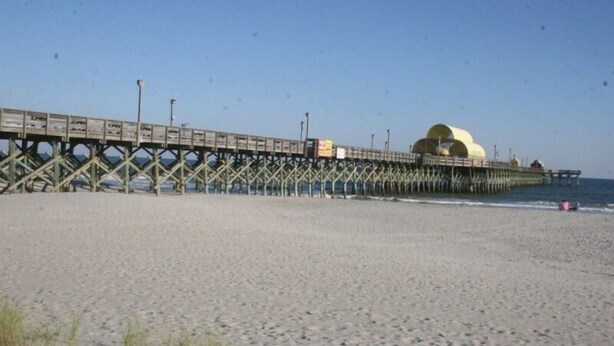A beach with a wooden pier extending into the ocean, featuring a large dome structure at the end. - Lake Arrowhead Layaway (Myrtle Beach)