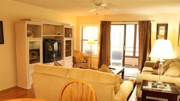 Una sala de estar con un sofá, un televisor, una mesa de comedor y un arreglo floral, además de una lámpara.