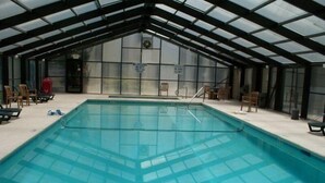 Una piscina interior con techo de vidrio, rodeada de sillas de descanso y un letrero que indica una profundidad de 1.8 metros.