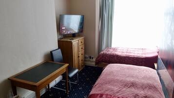 A hotel room with a bed, a desk with a chair, a television on a wooden dresser, and a window with curtains.
