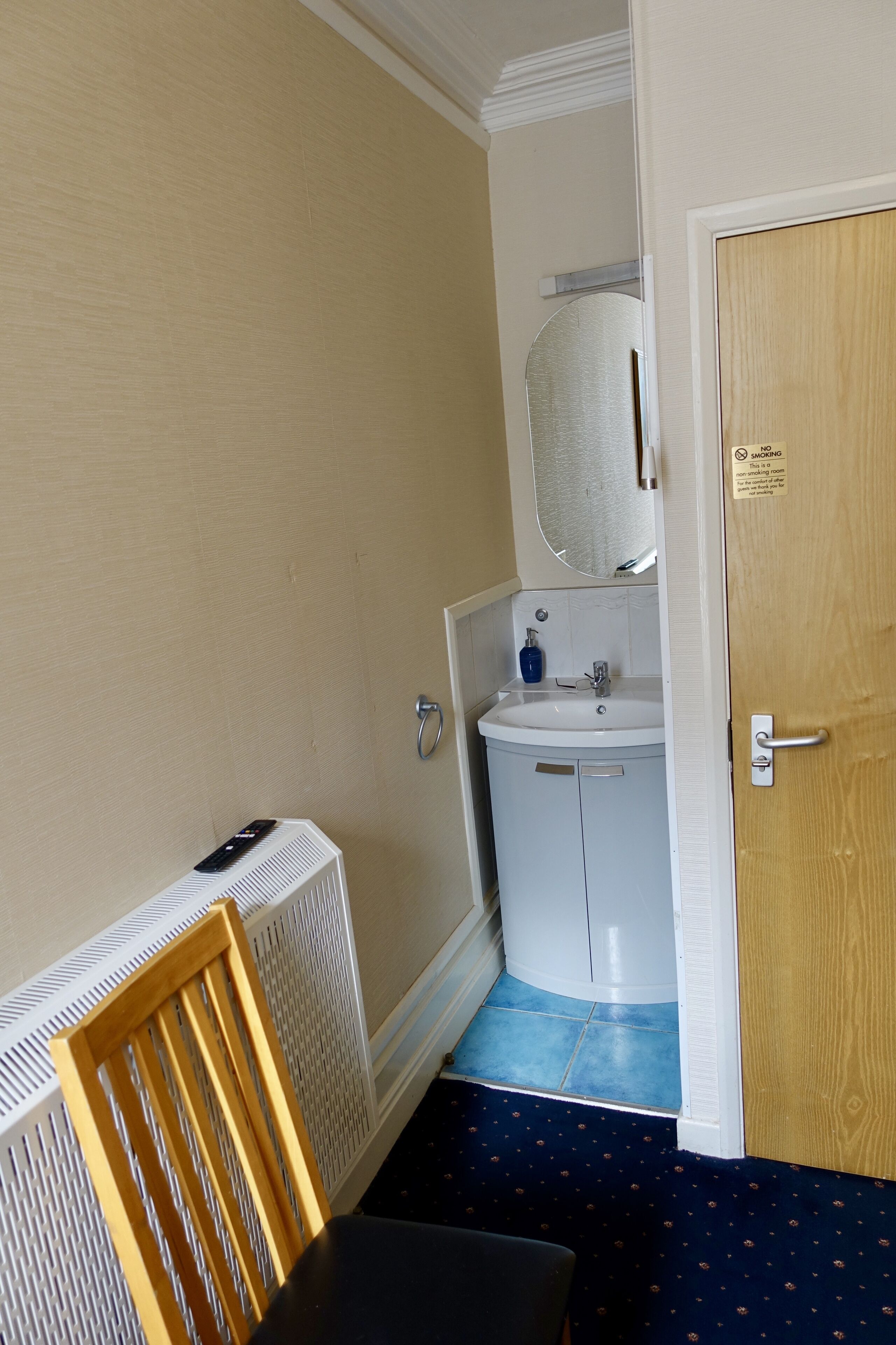 A small bathroom with a white sink, a mirror, and a wooden chair.