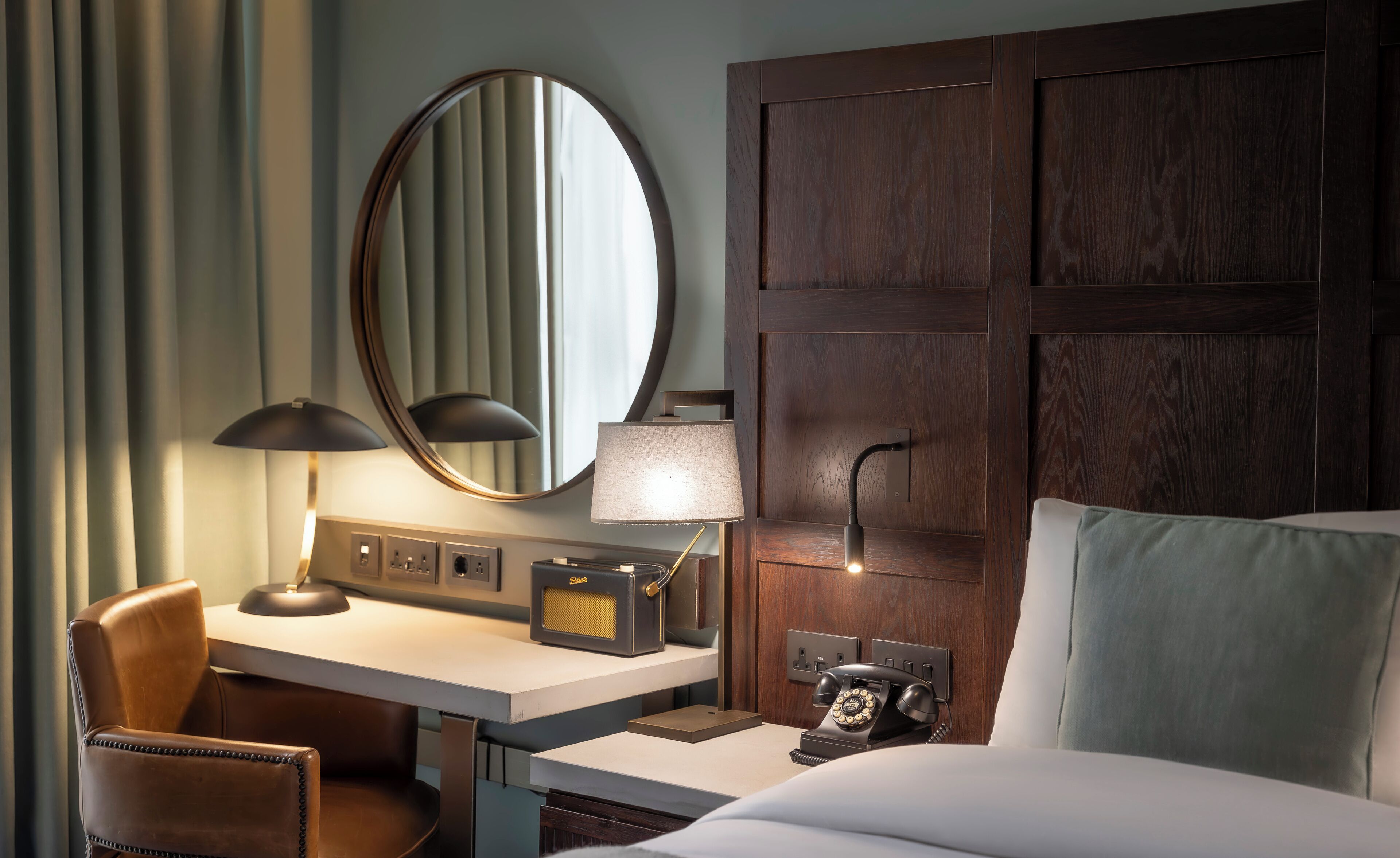 Une chambre d’hôtel avec une tête de lit en bois, un bureau avec une lampe, une chaise, un lit avec un oreiller et un téléphone.