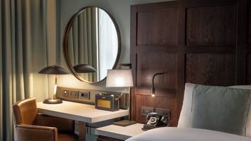 A hotel room with a wooden headboard, a desk with a lamp, a chair, a bed with a pillow, and a telephone.