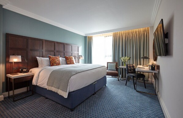 A hotel room with a large bed, a desk, a chair, a TV, and a window with curtains. - Clayton Hotel Cambridge (Cambridge)