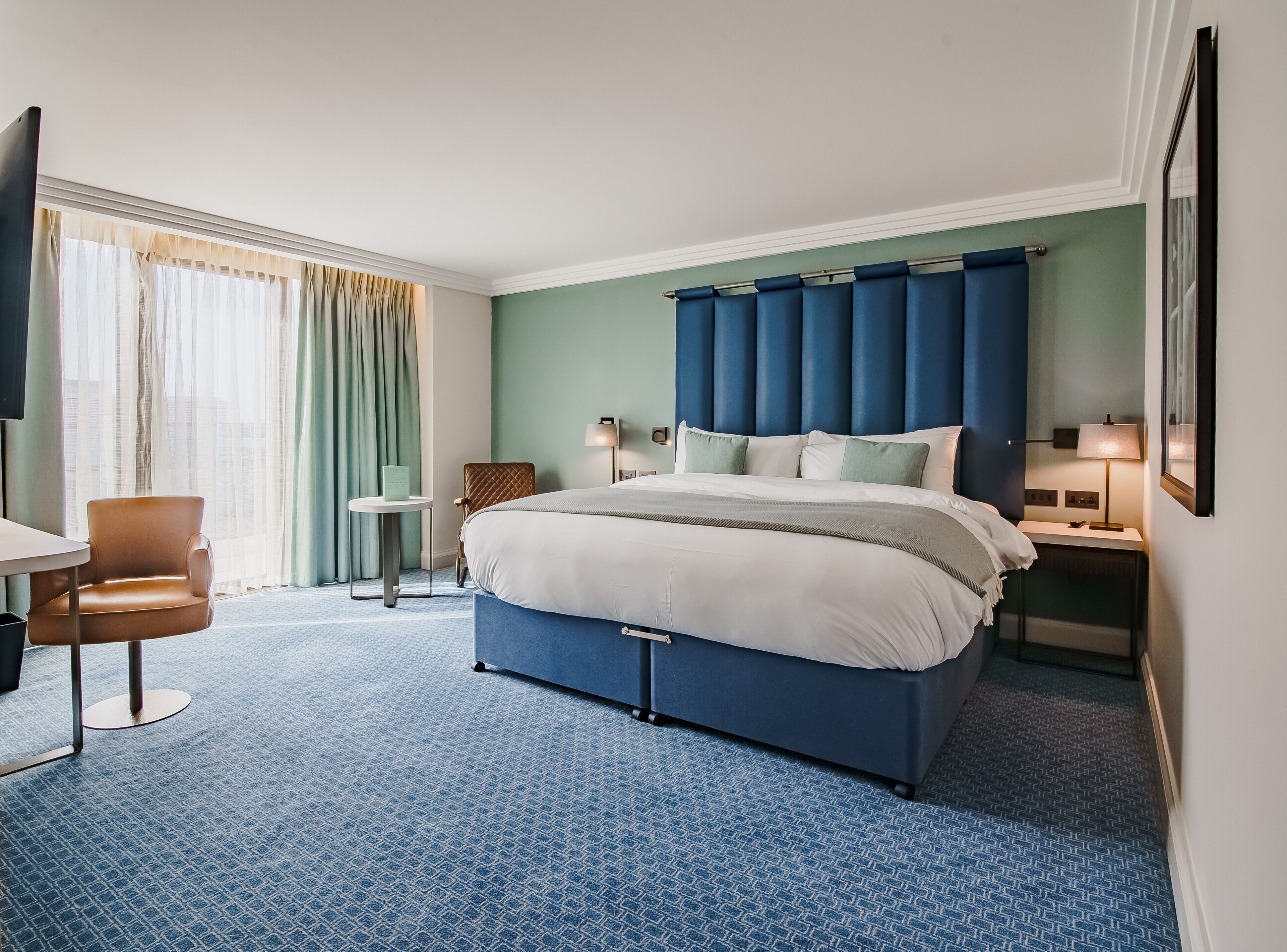 Une chambre d’hôtel avec un grand lit, une chaise, une petite table et une table de chevet avec une lampe.
