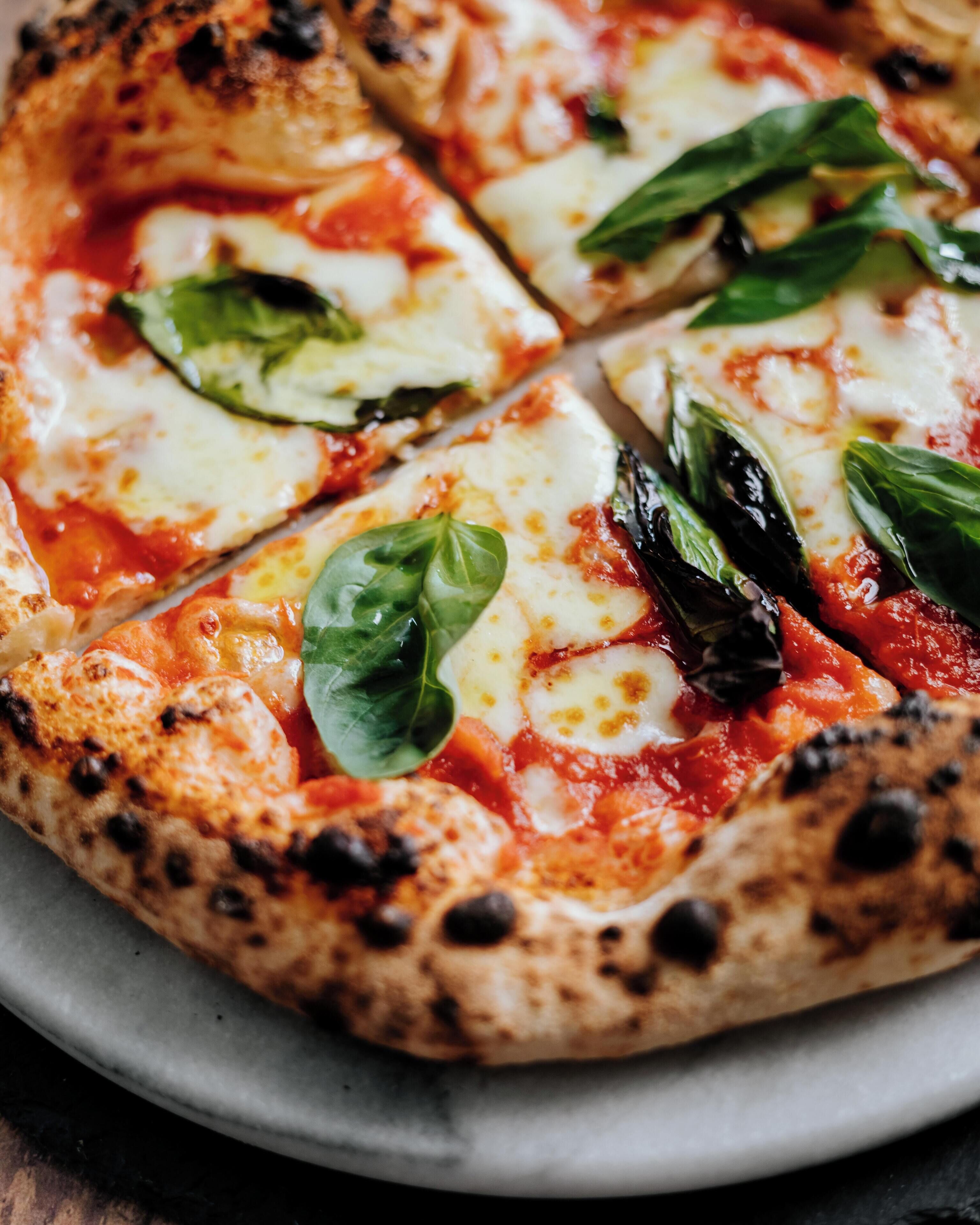 A pizza with cheese, tomato sauce, and basil leaves on a plate.
